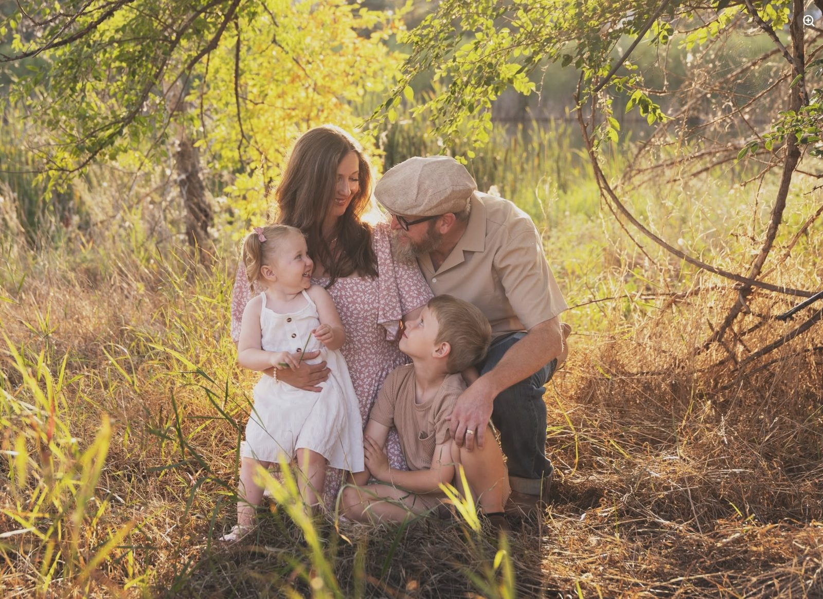 The family behind Next to Kin — two parents and their two young children, outdoors in tall grass at golden hour.
